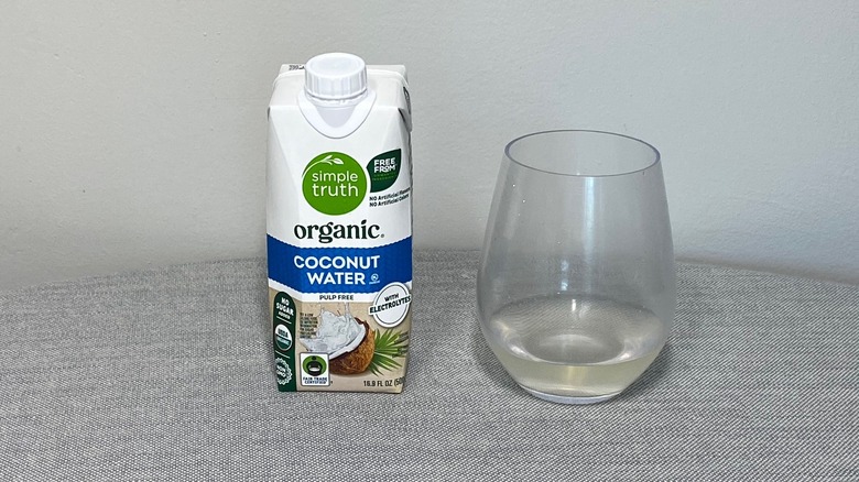 A carton of Simple Truth coconut water on a table beside a glass of the product