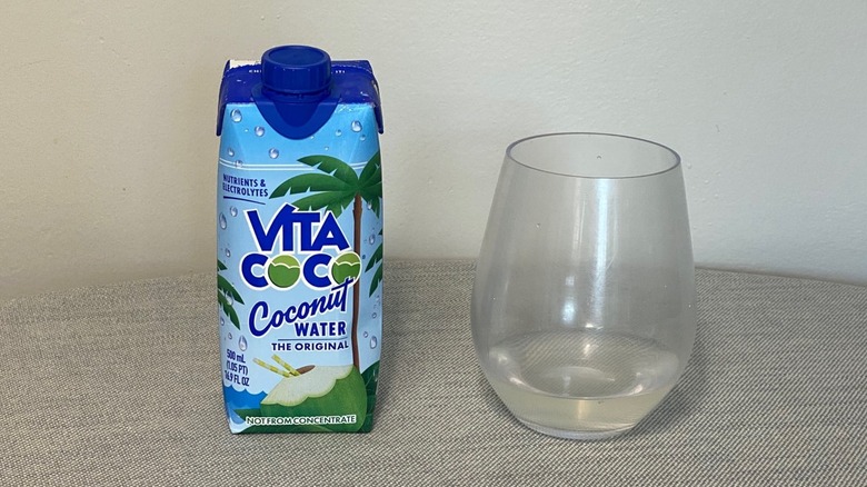 A carton of Vita Coco coconut water on a table beside a glass of the product