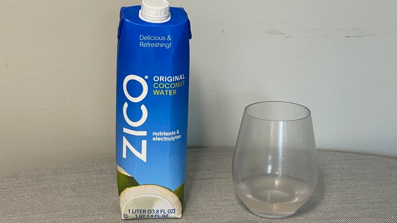 A carton of Zico coconut water on a table beside a glass of the product