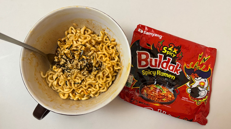 Bowl of Buldak 2X Spicy noodles and its original packaging on white surface