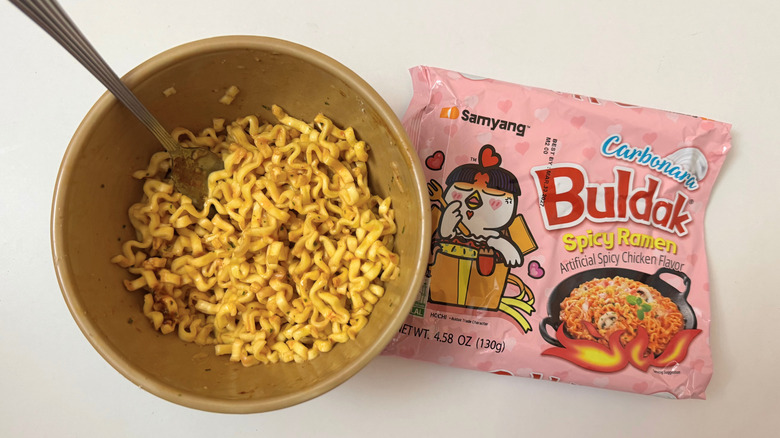 Bowl of Buldak Carbonara noodles next to its original packaging on white surface