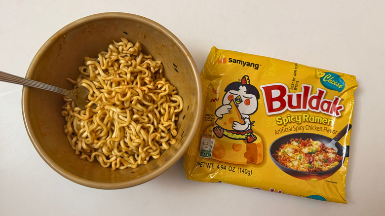 Bowl of Buldak Cheese noodles and its original packaging on white surface