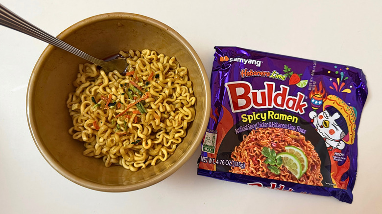 Bowl of Buldak Habanero Lime noodles and its original packaging on white surface