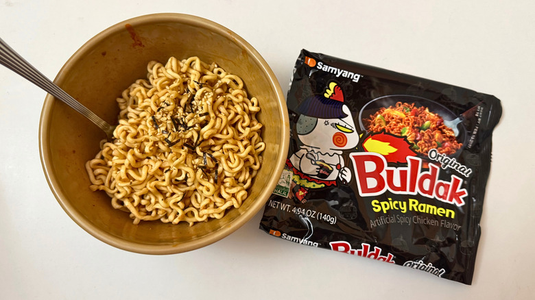 Bowl of Buldak Original Hot Chicken Flavor noodles next to its original packaging on white surface