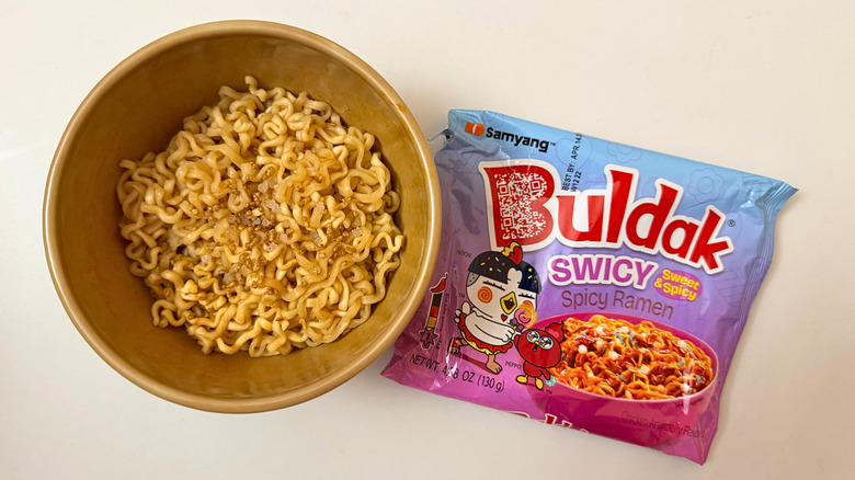 Bowl of Buldak Swicy noodles next to its original packaging on white surface