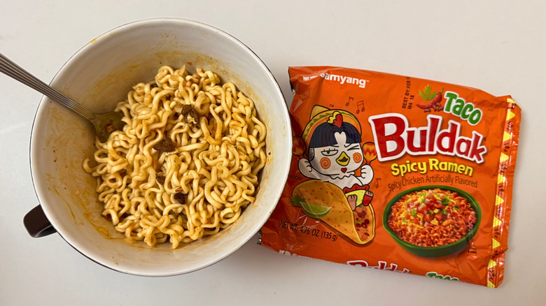 Bowl of Buldak Taco noodles and its original packaging on white surface