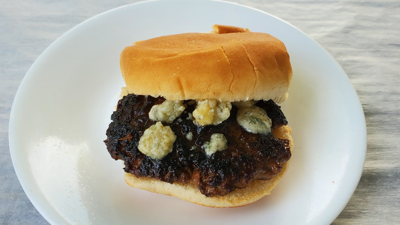 A beef slider with blue cheese crumbles on a white plate