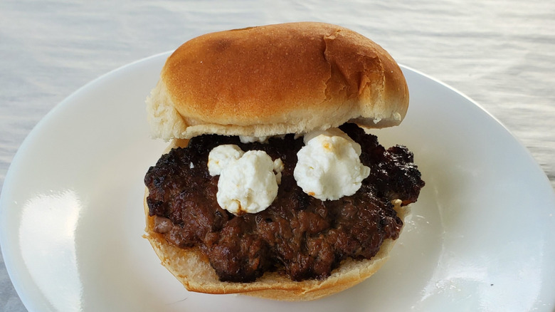 A beef slider with goat cheese crumbles on a white plate