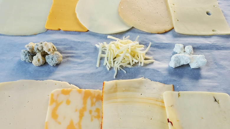 An assortment of sliced, shredded, and crumbled cheeses arranged on white parchment paper