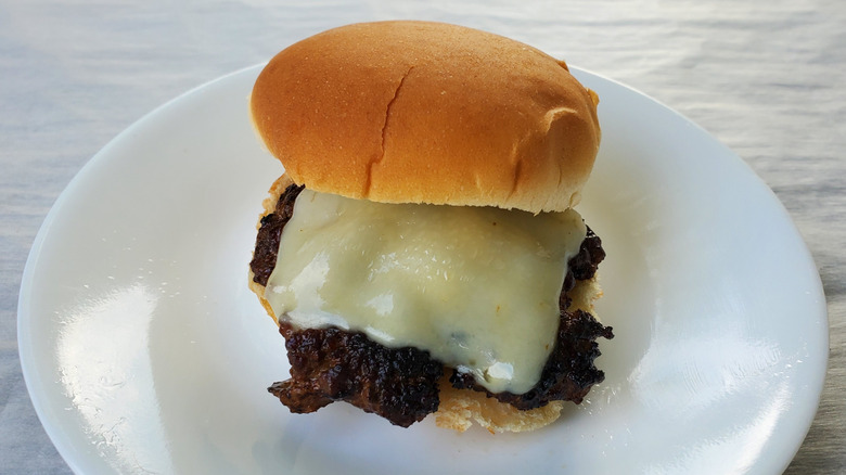 A beef slider with Swiss cheese on a white plate