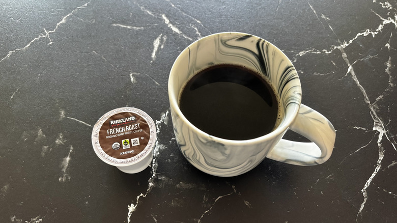 Kirkland French roast coffee pod next to brewed cup of coffee