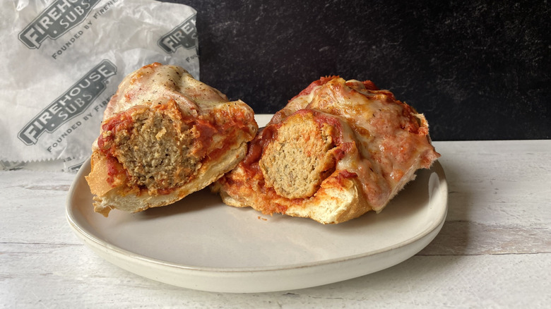 A Firehouse meatball sub sliced in half on a plate in front of the to-go wrapping