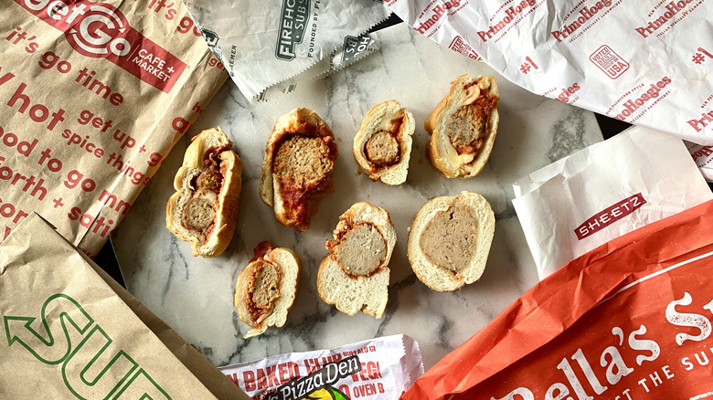 Slices of seven different meatball subs on a marble slab surrounded by takeout bags