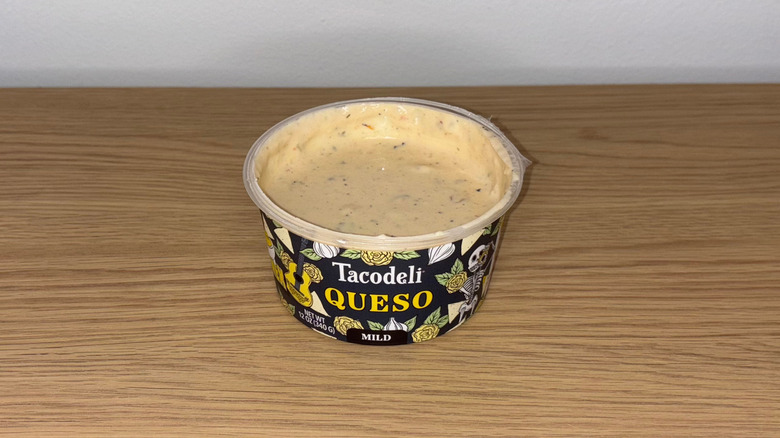 Container of Tacodeli Queso on a wood table.