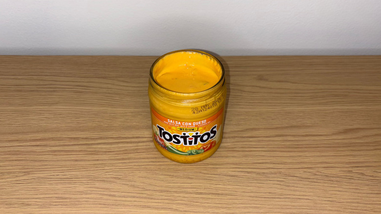 Glass jar of Tostitos Salsa Con Queso on a wood table.