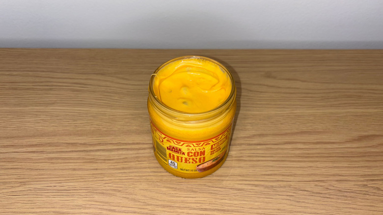 Glass jar of Casa Mamita Salsa Con Queso on a wood table.