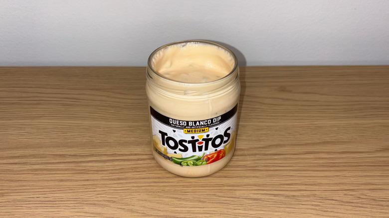 Glass jar of Tostitos Queso Blanco on a wood table.