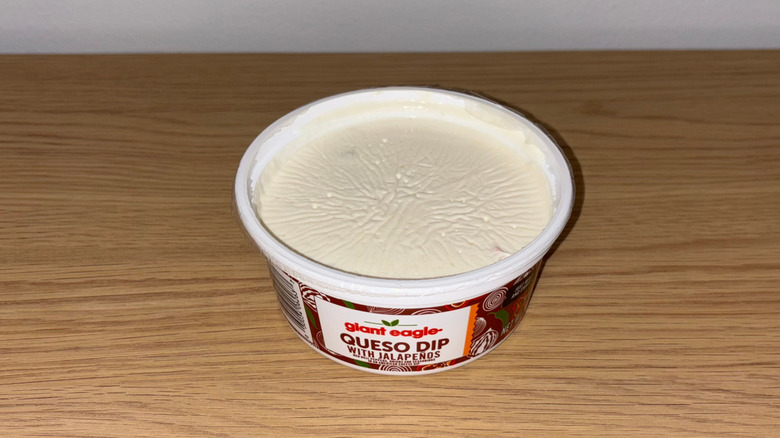 Plastic container of Giant Eagle Queso Dip on a wood table.