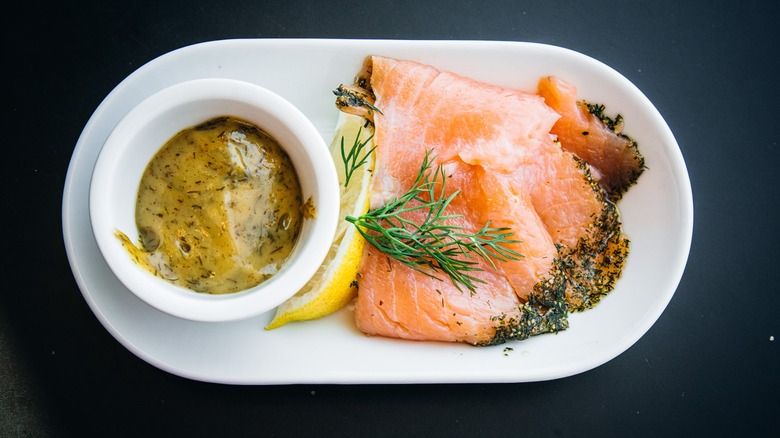 Two slices of IKEA Marinated Salmon on a small white plate with lemon, dill, and honey mustard dill sauce
