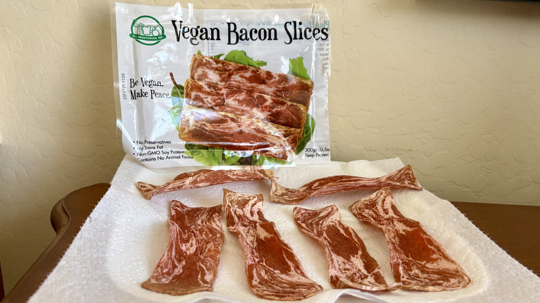 A plate of prepared All Vegetarian Inc Vegan Bacon Slices in front of its packaging