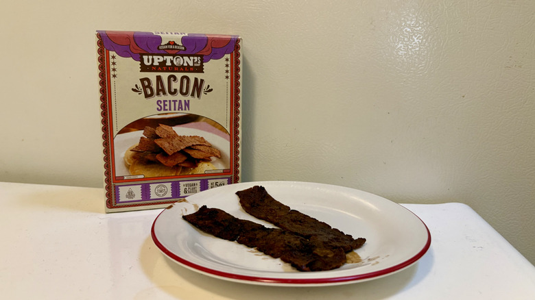 A plate of prepared Upton's Naturals Seitan Bacon in front of its packaging