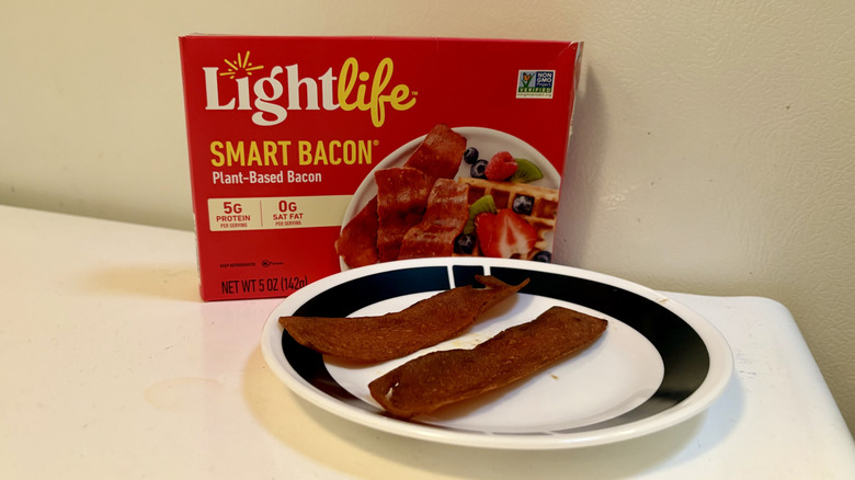 A plate of prepared LightLife Bacon in front of its packaging
