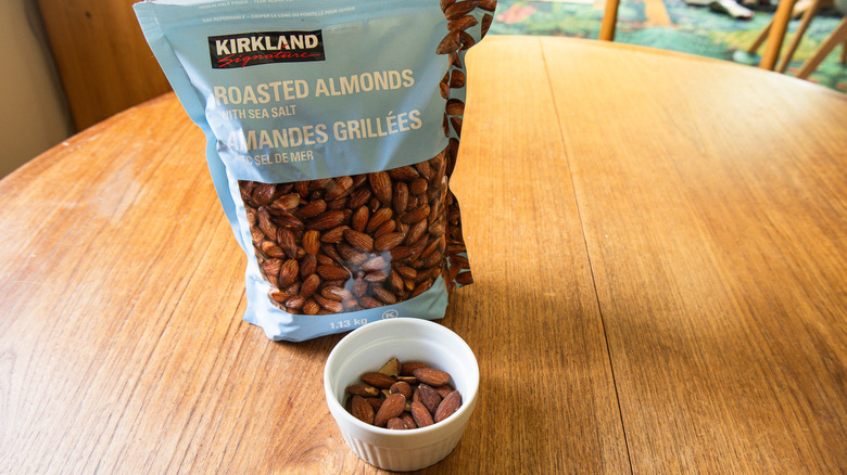 A bag of Kirkland Roasted Almonds with Sea Salt beside a ramekin with nuts.