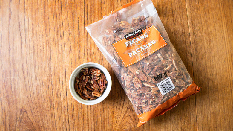 A bag of Kirkland Signature Pecan Halves with Salt beside a ramekin with nuts.