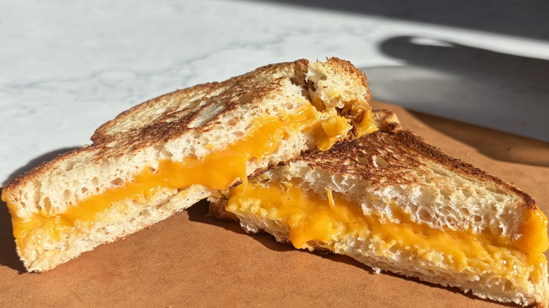 A halved grilled cheese sandwich made with American cheese sits on a cutting board