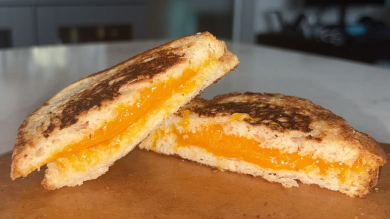 A halved grilled cheese sandwich made with extra sharp cheddar cheese sits on a cutting board