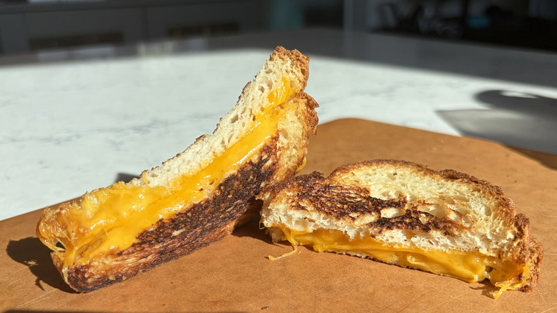A halved grilled cheese sandwich made with medium cheddar cheese sits on a cutting board