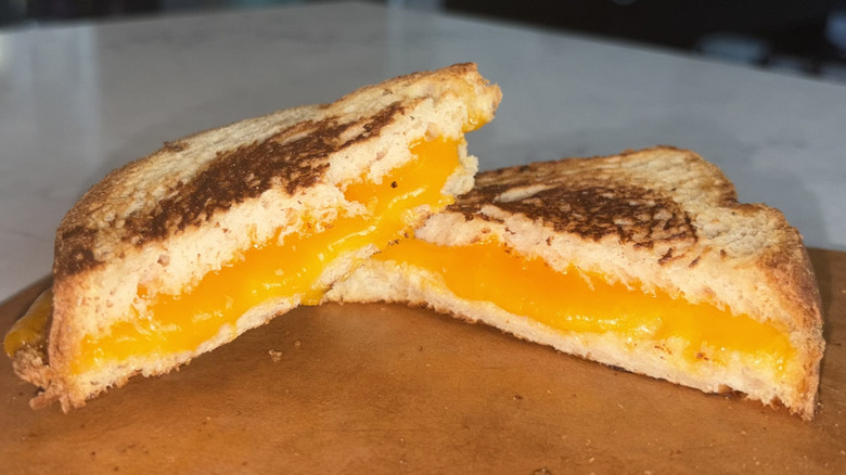 A halved grilled cheese sandwich made with mild cheddar cheese sits on a cutting board