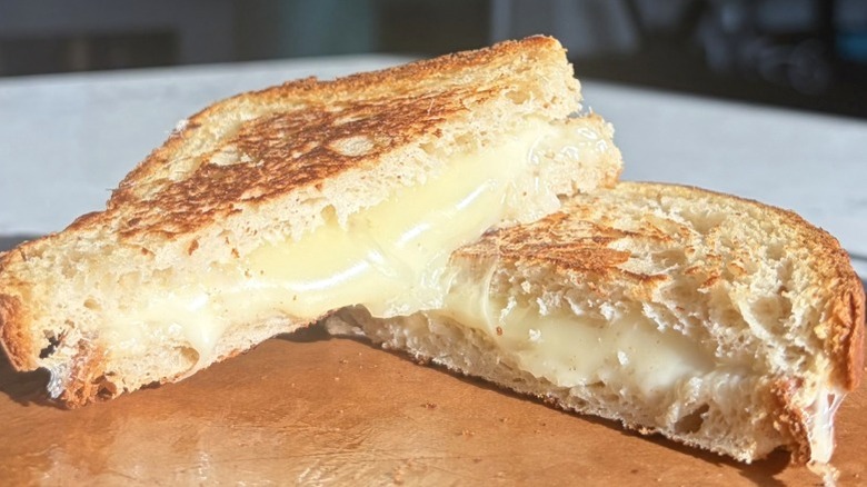 A halved grilled cheese sandwich made with mozzarella cheese sits on a cutting board