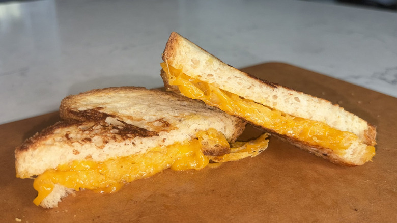 A halved grilled cheese sandwich made with sharp cheddar cheese sits on a cutting board
