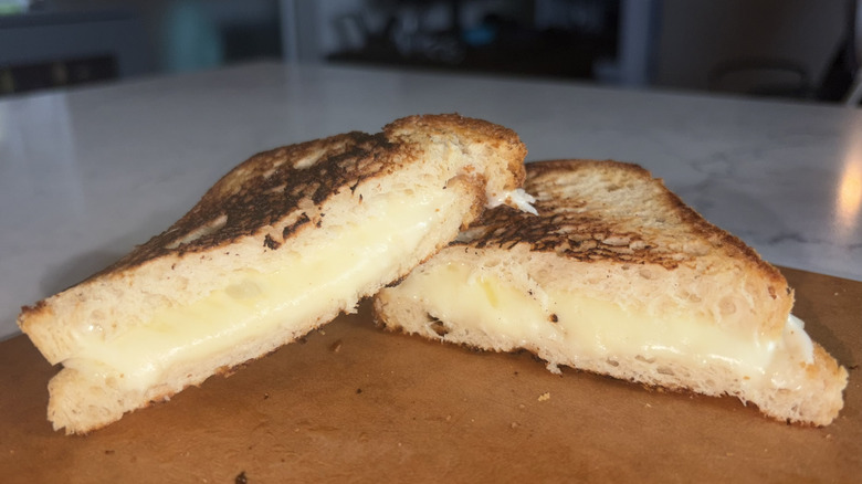 A halved grilled cheese sandwich made with smoked provolone cheese sits on a cutting board