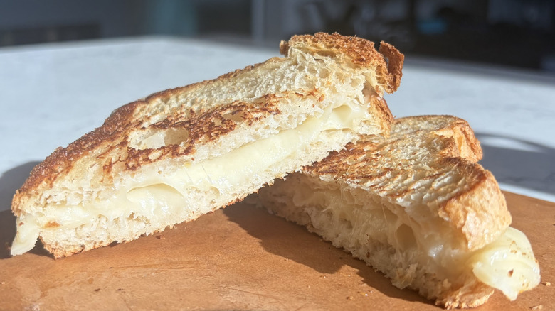 A halved grilled cheese sandwich made with Swiss cheese sits on a cutting board