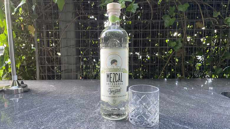 Gracias a Dios Tepextate mezcal bottle and glass tumbler sit on an outdoor counter.