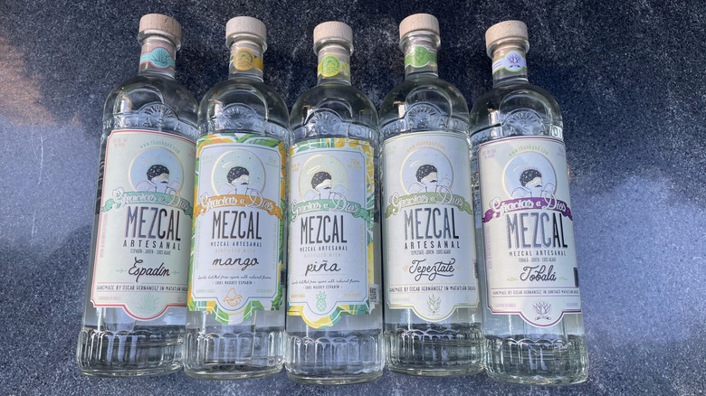 All five Gracias a Dios reviewed bottles lay flat on a stone countertop.