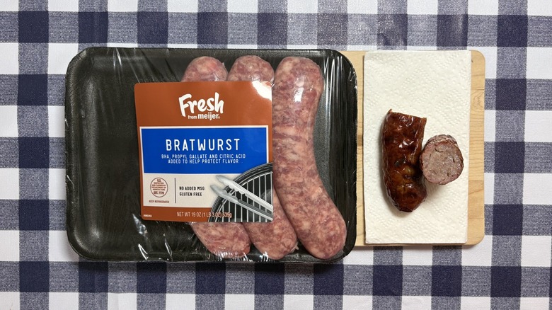Meijer bratwurst package next to cooked brat cut in half on checkered tablecloth