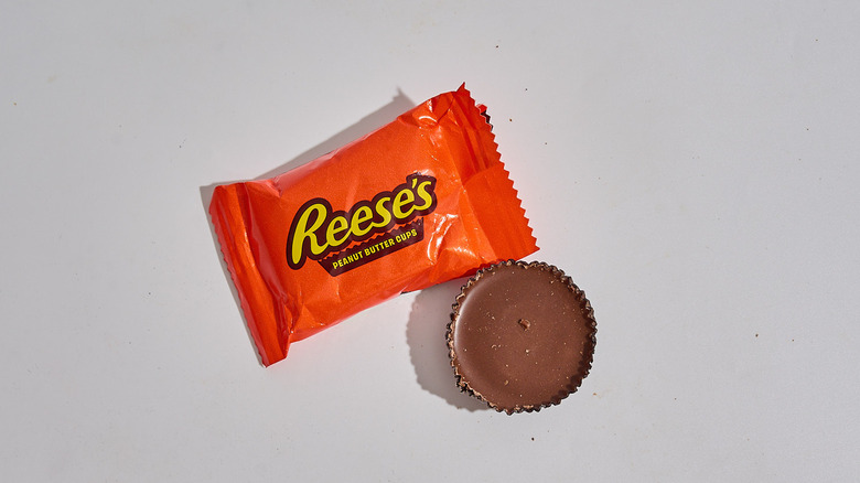 A package of Reese's Peanut Butter Cups on a table with a Peanut Butter Cup out of the package