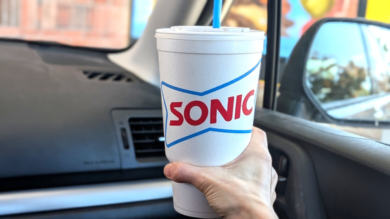 A hand holding a Sonic Diet Coke in a car