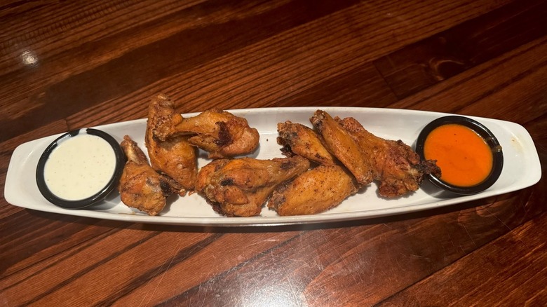 White dish filled with chicken wings and two cups of sauce on wooden table.