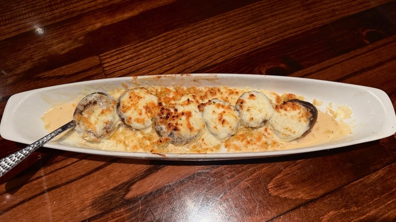 White dish filled with cheese-stuffed mushrooms and spoon on wooden table.