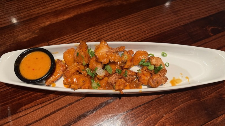 White dish filled with spicy chicken pieces and cup of sauce on wooden table.