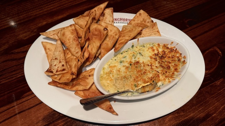 White dish with flatbread chips and bowl of spinach dip on wooden table.
