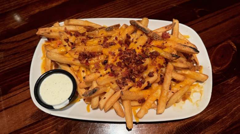 White dish filled with loaded cheese and bacon fries on wooden table.