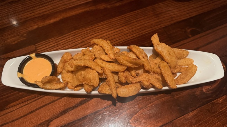 White dish filled with fried onion pieces and cup of sauce on wooden table.