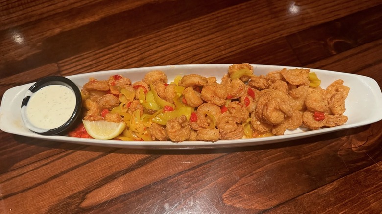 White dish filled with breaded shrimp and cup of ranch on wooden table.