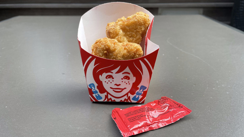 Two Wendy's nuggets sit in a french fry container on a table with a ketchup packet.
