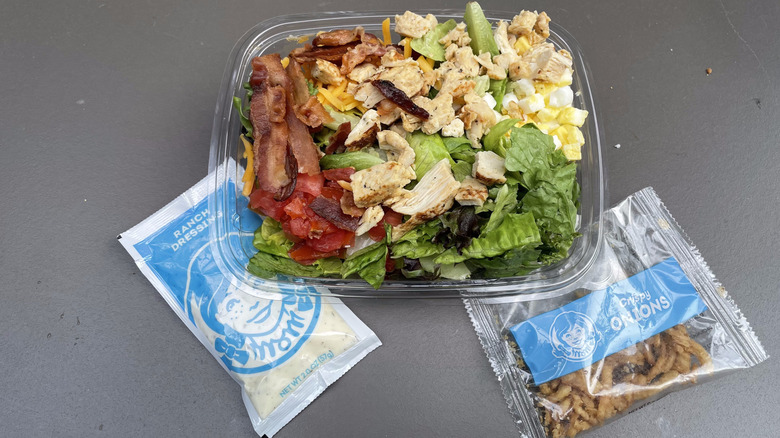 A Wendy's Cobb salad sits on a table with a ranch dressing packet and a crispy onion packet.